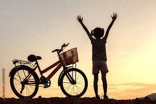 Silhouette of child raised hands with bike standing on mountain