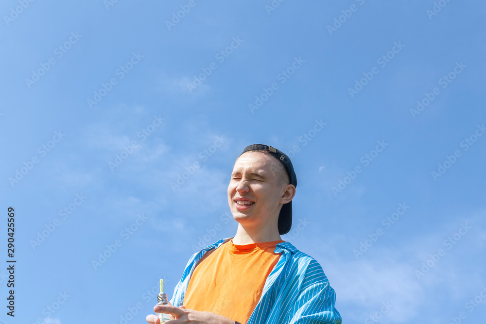 The guy squints with laughter against the blue sky The guy squints with laughter against the blue sky