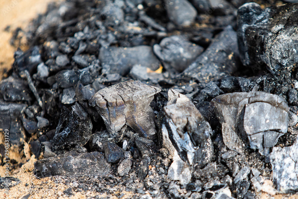 Black coals after a fire on a sandy shore.