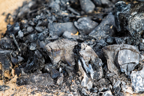 Black coals after a fire on a sandy shore.