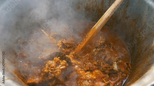 slow motion of cooking lamb stew with wooden spoon in big cauldron photo