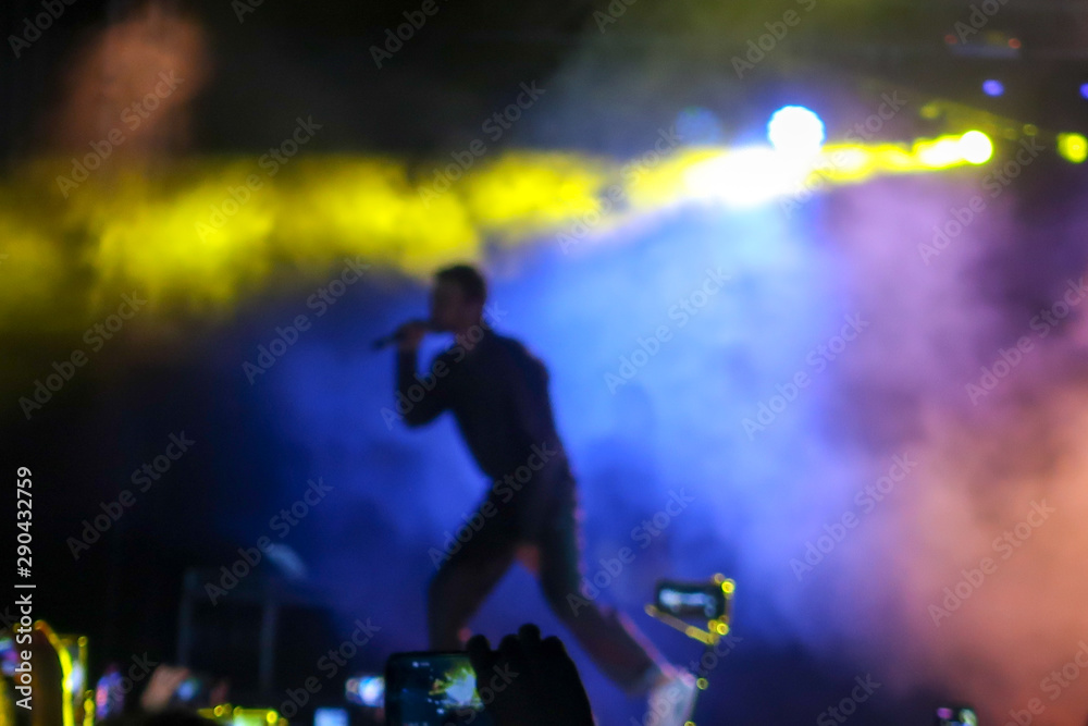 Blurred background to place text. Blurred Music Festival Background of a large hip hop concert in a nightclub. Bright stage lighting, a crowded dance floor with music lovers enjoy the show.