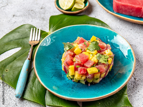 Tropical style gourmet tuna mango salad tartar with cilantro and purple onion. On blue plate, tropical leaves photo