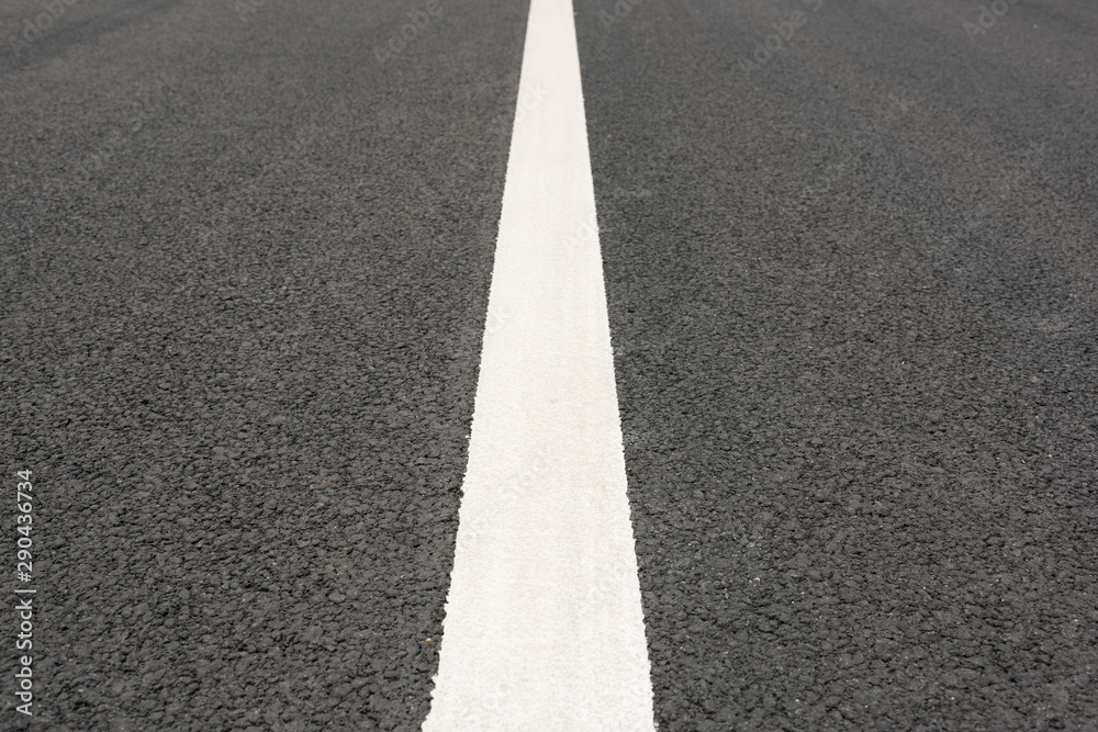 Low angle view of a white paint line closeup in the middle of asphalt road