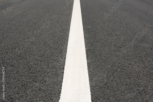 Low angle view of a white paint line closeup in the middle of asphalt road © bqmeng