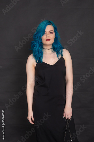 People and fashion concept - Woman dressed in black dress and blue hair posing over black background