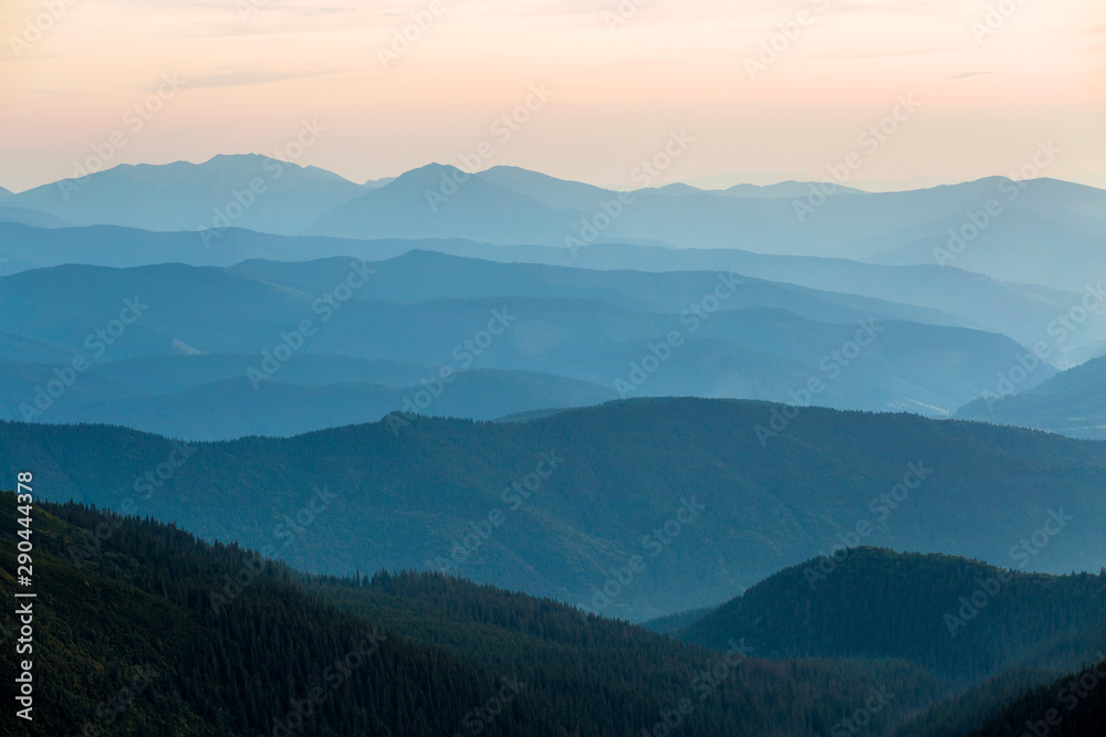 Landscape view of green majestic Carpathian mountains covered with light mist in dawn.