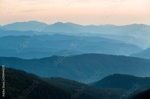 Landscape view of green majestic Carpathian mountains covered with light mist in dawn.