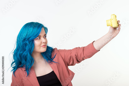 People  hobby and interests concept - Beautiful girl with blue hair hold yellow retro camera on white background