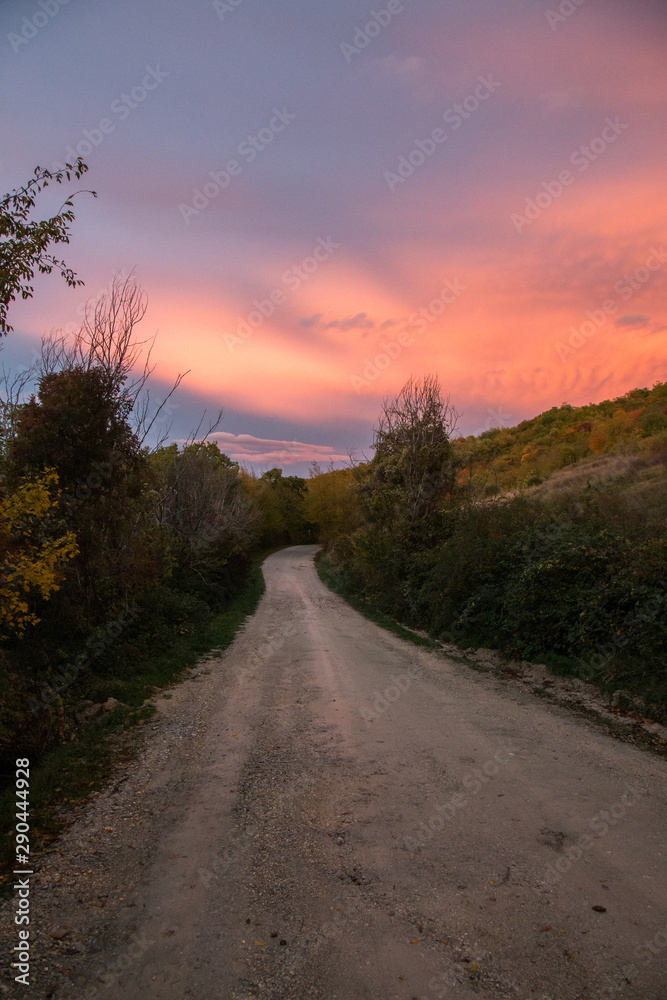 A mountain road below orange and yellow coloured clouds at sunset