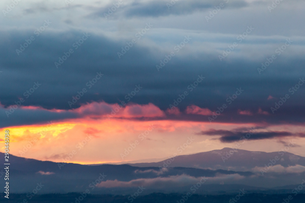 View of colorful clouds at sunset, over and below a mountain