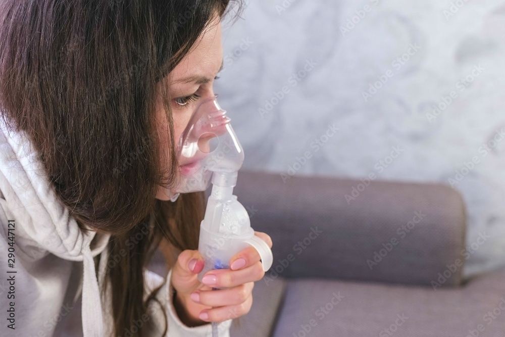 Use nebulizer and inhaler for the treatment. Young woman inhaling through inhaler mask, face close-up, side view Use nebulizer and inhaler for the treatment. Young woman inhaling through inhaler mask, face close-up, side view
