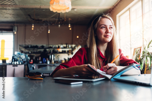 Pretty and dreamy woman working in cozy work space with paperwork, wearing red smart-casual dress