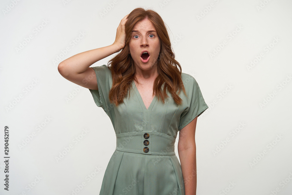 Indoor shot of surprised young woman with curly red hair, looking to camera with wide mouth opened, keeping palm on her head, isolated over white background Indoor shot of surprised young woman with curly red hair, looking to camera with wide mouth opened, keeping palm on her head, isolated over white background