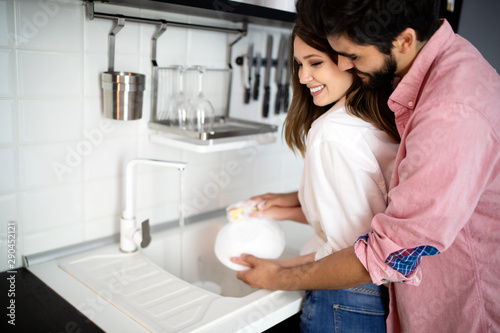 Obraz na plátně Young couple doing dishes in the kitchen while hugging and having fun