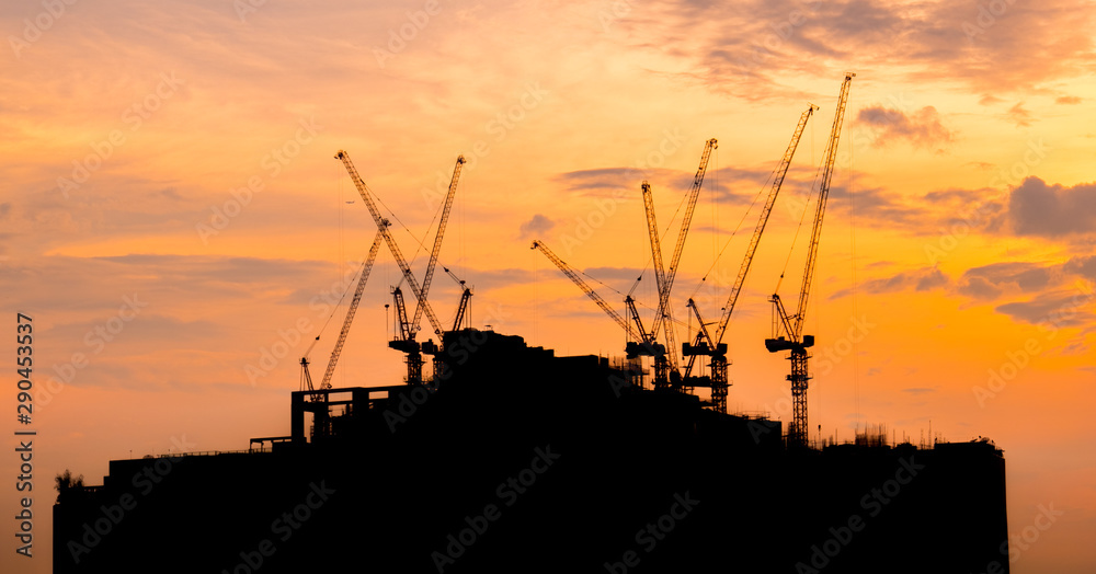 Silhouette building under construction with crane over sunset background