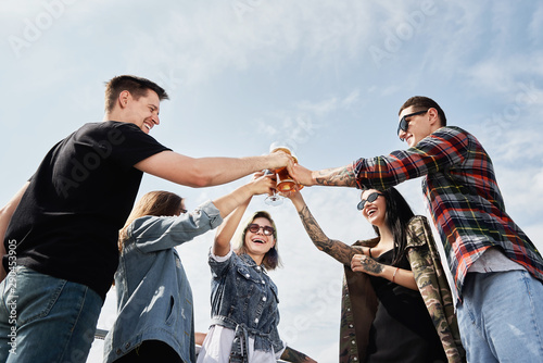 Group of friends drinking beer before festival at outdoors pub on roof, toasting and laughing, copy space. Friendship and celebration concept photo