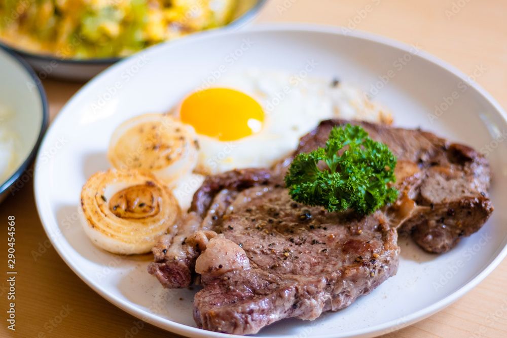 Close up and selective focus of meat beef steak Fried egg and onion in white plate on wooden table.