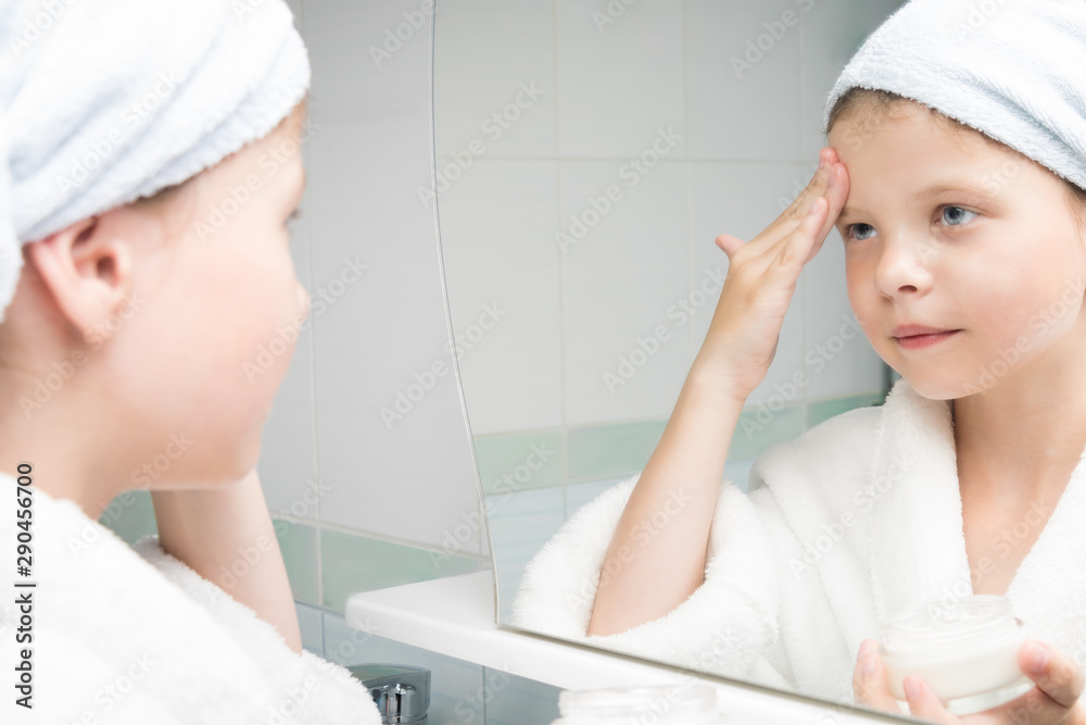 girl in a white coat moisturizes her face with cream girl in a white coat moisturizes her face with cream