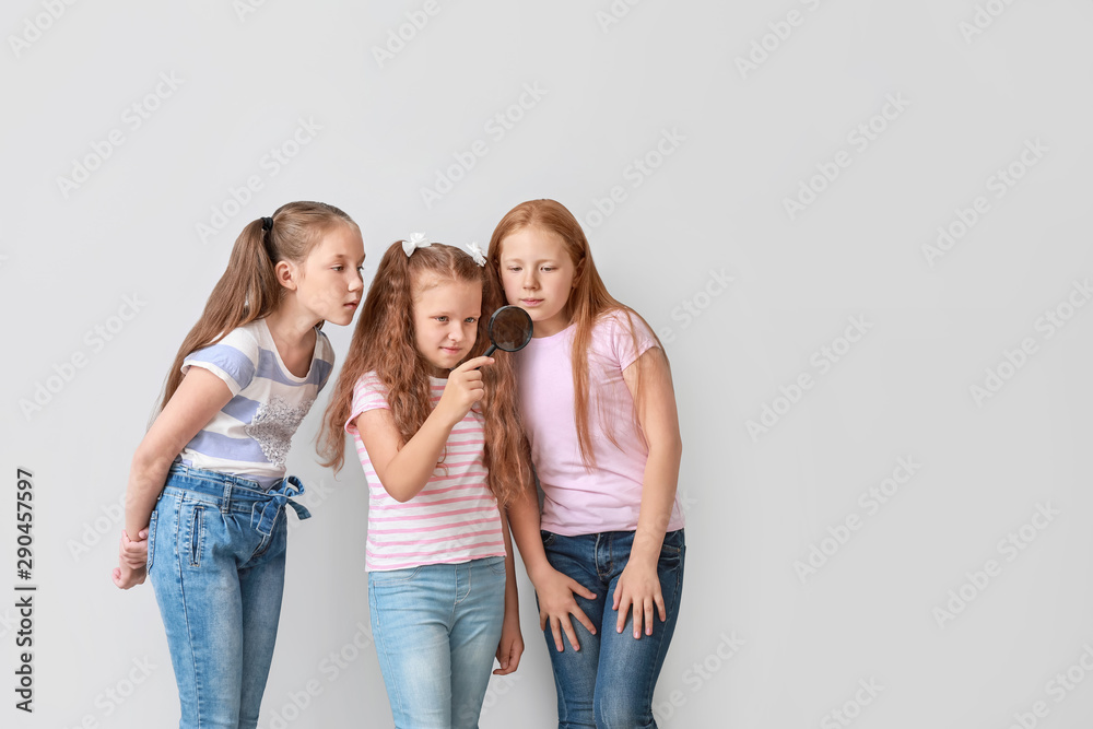 Obraz premium Little girls with magnifying glass on light background