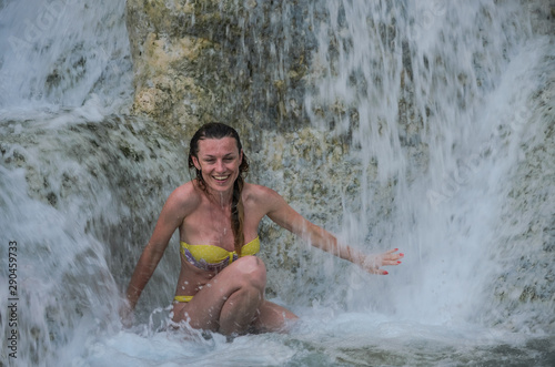 Young charming girl in a bikini swimsuit under the streams of a waterfall