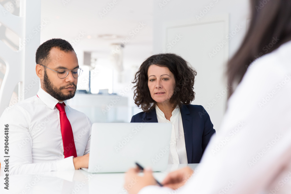 Employers interviewing job applicant. Business man and woman sitting at conference table with open laptop, and talking to employee sitting opposite. Career concept