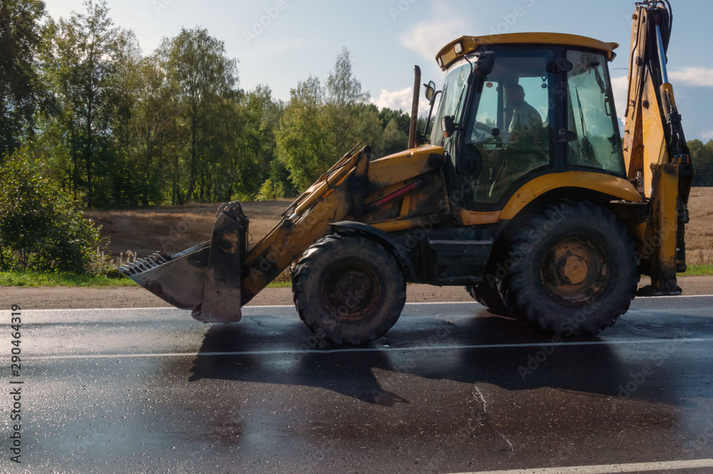 An excavator tractor rides after field work on an asphalt road. An excavator tractor rides after field work on an asphalt road.