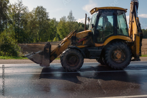 An excavator tractor rides after field work on an asphalt road.