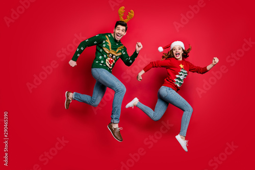Full length photo of crazy jumping couple excited by x-mas discounts prices wear ugly ornament jumpers isolated red color background