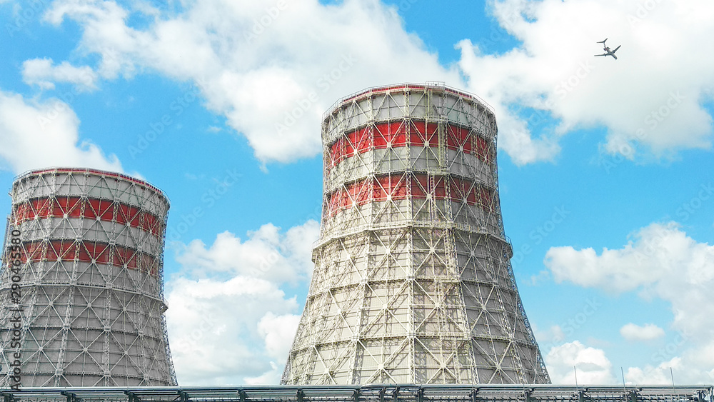 Pipes of a thermal power plant with a flying plane against the sky with clouds