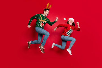 Full body photo of amazed jumping couple excited by x-mas prices hurry shopping wear ugly ornament jumpers isolated red color background