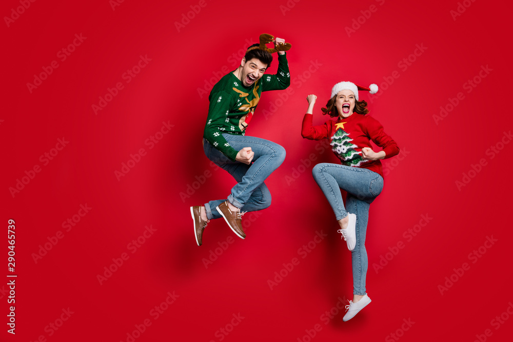 Full body photo of amazed jumping couple excited by x-mas prices wear ugly ornament jumpers and headwear isolated red color background - obrazy, fototapety, plakaty 