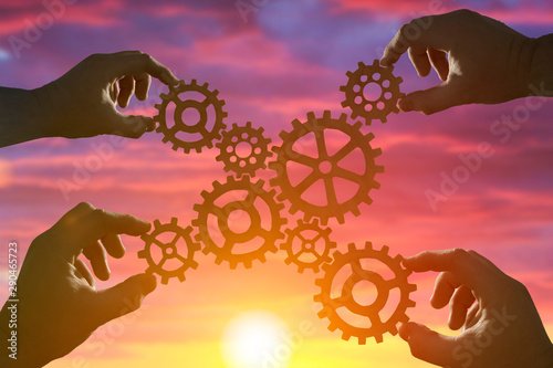 Hands of businessmen connect gears to puzzle on sunset background. Concept business ideas, cooperation, partnership, teamwork, innovation.