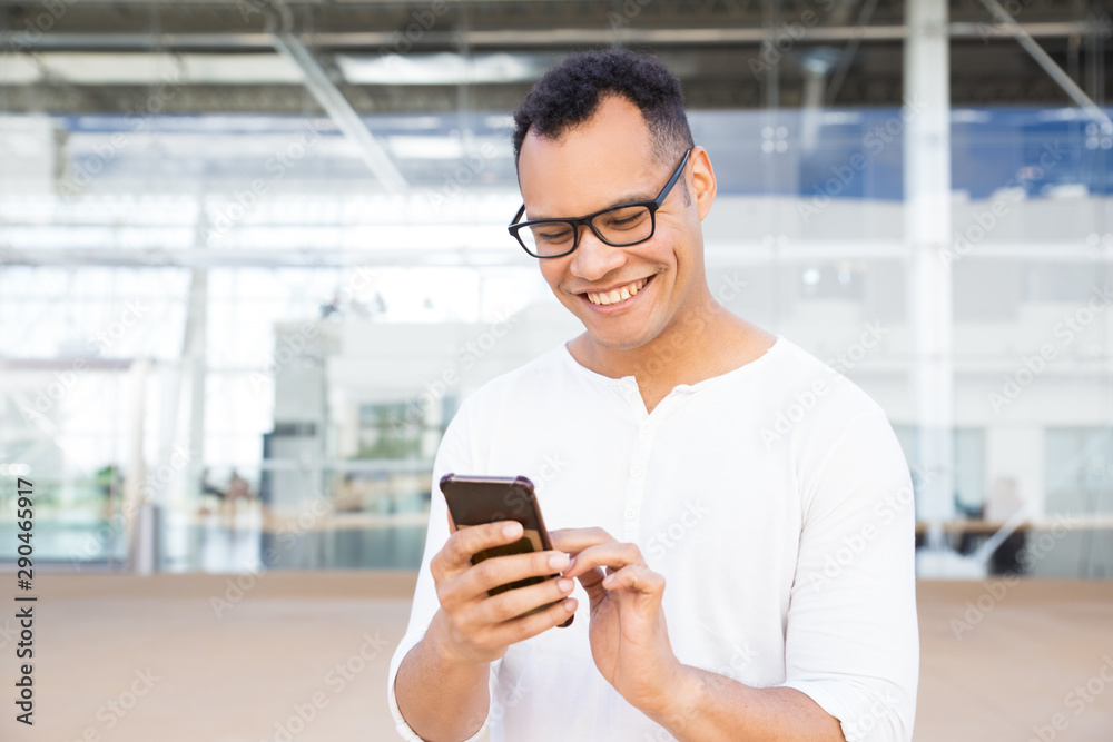 Smiling African American young man using smartphone. Front view of handsome young guy holding modern phone. Technology concept Smiling African American young man using smartphone. Front view of handsome young guy holding modern phone. Technology concept
