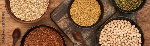 panoramic shot of bowls with buckwheat, chickpea and beans near spoons on wooden cutting boards