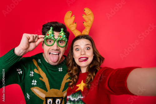 Photo of childish lady and guy at x-mas costume party making selfies wear ugly knitted pullovers isolated red color background