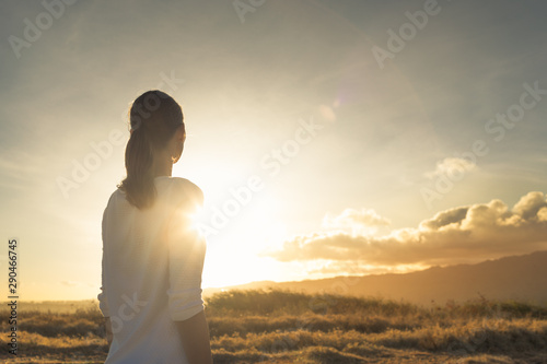 Looking to the future, new day, new beginning. Young female standing on a mountain facing sunset. 