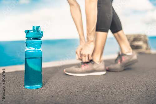 Female runner tying shoes next to bottle of water. Drinking water and fitness concept. 