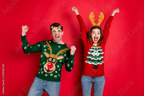 Portrait of crazy funny two family wife husband brown hair celebrate victory raise fists scream yes wear christmas tree design pullover jeans costume spectacles isolated over red color background