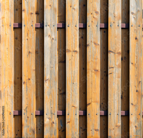 An unusual rustic old fence made of natural wooden spotted boards fixed on a brown metal bar with self-tapping screws. Abstract trendy texture background