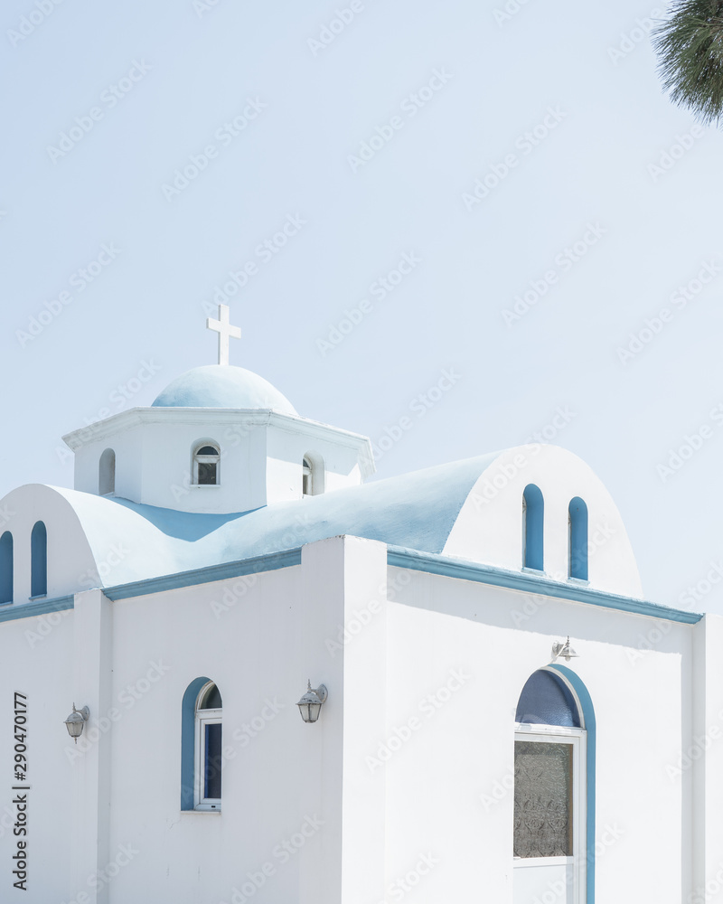 Traditional Greek church againts a clear blue sky bathed in bright sunlight.