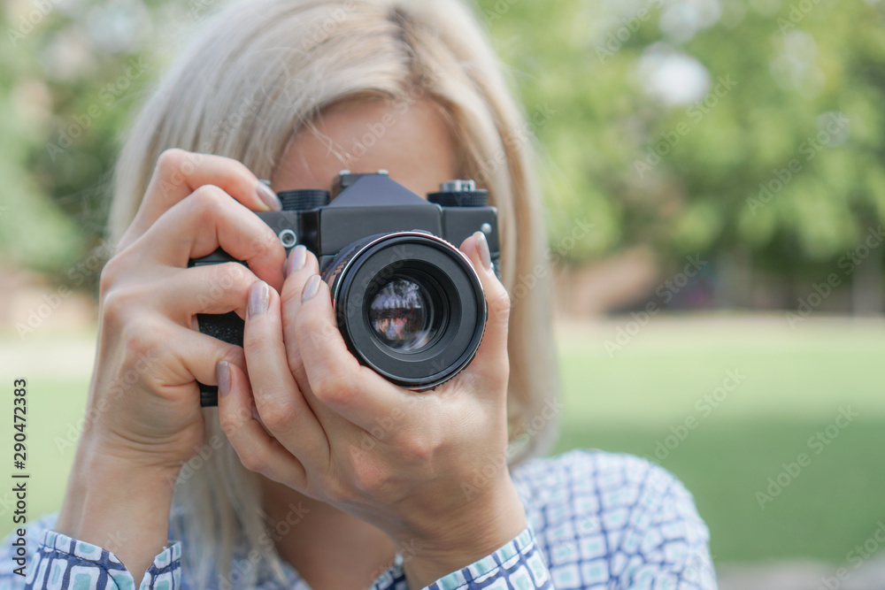 Girl blonde with a camera focuses in the park
