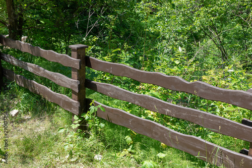 long wooden brown fence extend through a grass-filled field in the forest
