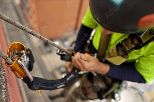 Rope access inspector industrial abseiler wearing full body safety abseiling harness using self controller stop fall descent safety backup device energy absorbing lanyard attached while abseiling 