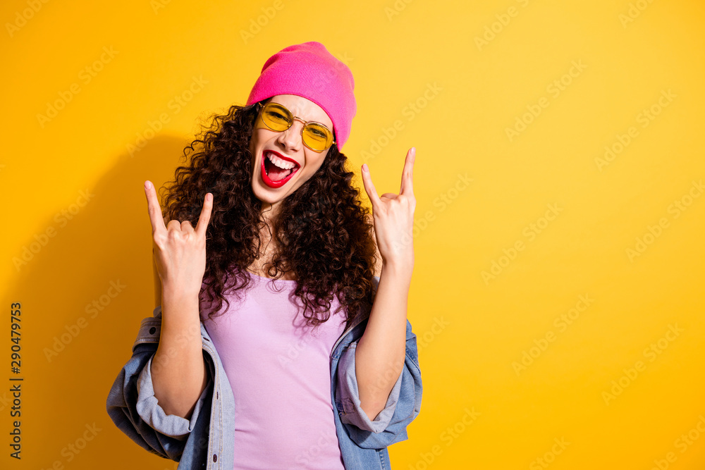 Portrait of excited cute girl show two fingers horned symbol celebrate punk event weekends wear spectacles modern denim jeans jacket pink tank-top isolated over yellow color background