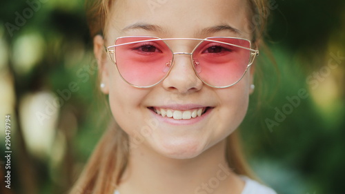 Portrait of a young smiling girl in pink transparent sunglasses outdoors. Close-up, soft focus.