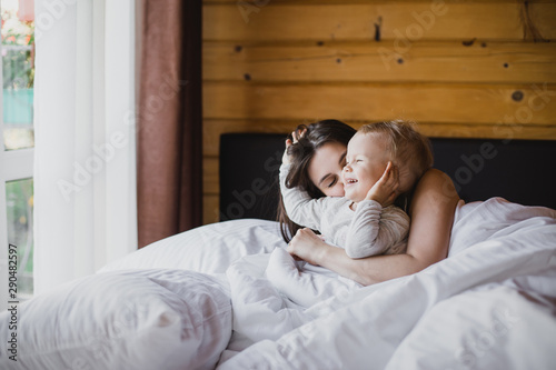Happy young mother and her baby playing in bed. © polinaloves