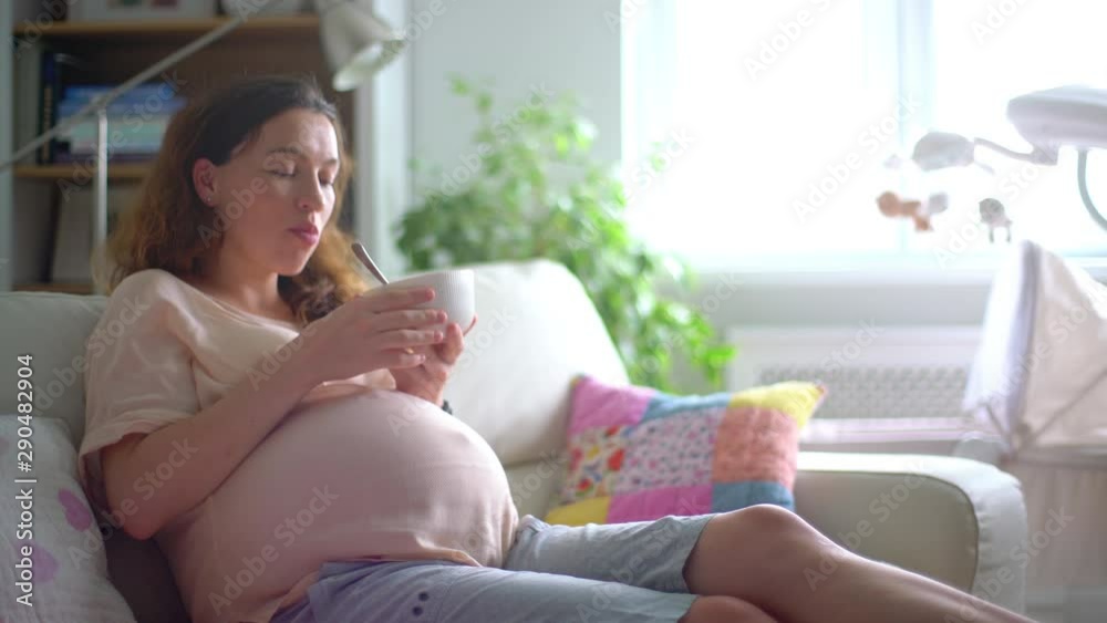 Portrait of a beautiful pregnant young woman sitting at sofa and eating healthy natural food at home Portrait of a beautiful pregnant young woman sitting at sofa and eating healthy natural food at home
