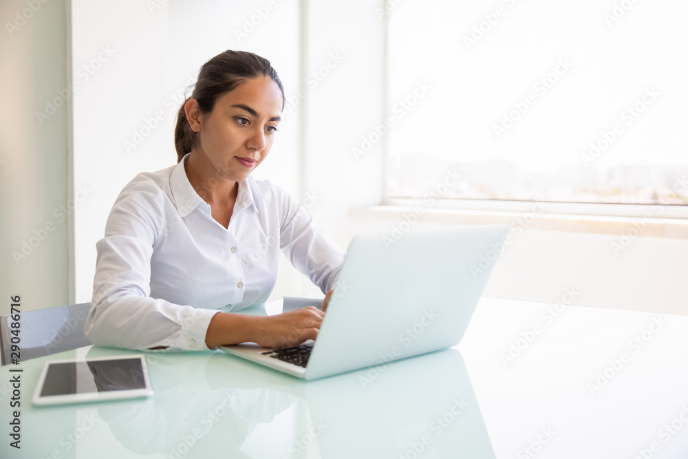 Focused female professional working on computer. Young Latin businesswoman sitting at workplace, using laptop, typing. looking at screen. Office worker concept Focused female professional working on computer. Young Latin businesswoman sitting at workplace, using laptop, typing. looking at screen. Office worker concept