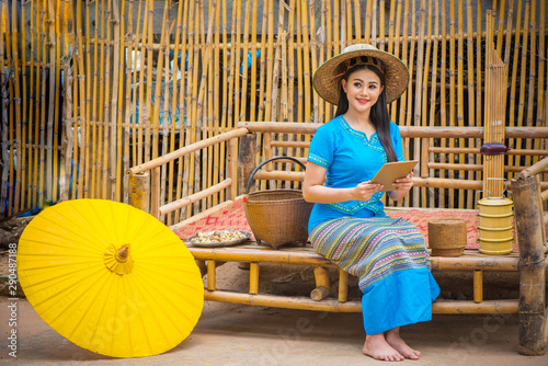 Asian women in blue local dresses using tablet or mobile device, Country life with yellow umbrella, tiffin carrier,Bamboo basket and Khene(Thai Musical Instruments), Technology in rural concept. photo
